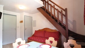 A dining area with a table set for four, a wooden staircase, and a red sofa.