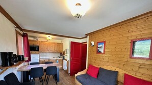 Ein gemütliches Blockhaus-Interieur mit einem Holzespeisetisch, Stühlen, einer Couch mit roten Kissen und einer Küchenzeile mit Holzausbau und einer roten Tür.