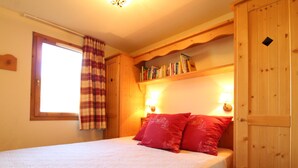Ein Schlafzimmer mit einem Bett, einem Fenster mit Vorhängen, einem Bücherregal und Wandlampen.