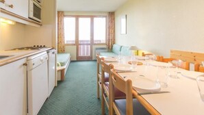 Eine kleine Küche mit Herd, Mikrowelle und Spüle. Ein Essbereich mit Tisch für zwei Personen, Stühlen und einer Bank.