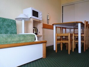 A small room with a green sofa, a wooden table with chairs, a white microwave, and a telephone on the wall. - 200m from ski slopes, 1st floor, view valley, balcony, tv, 35m², Montchavin La Plagne (Bellentre)