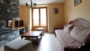 Uma sala de estar com parede de pedra, sofá de madeira, televisão, mesa e lustre.