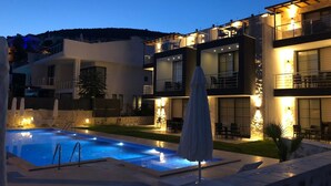 Un edificio moderno de varios pisos con piscina, mobiliario exterior y un patio cubierto.