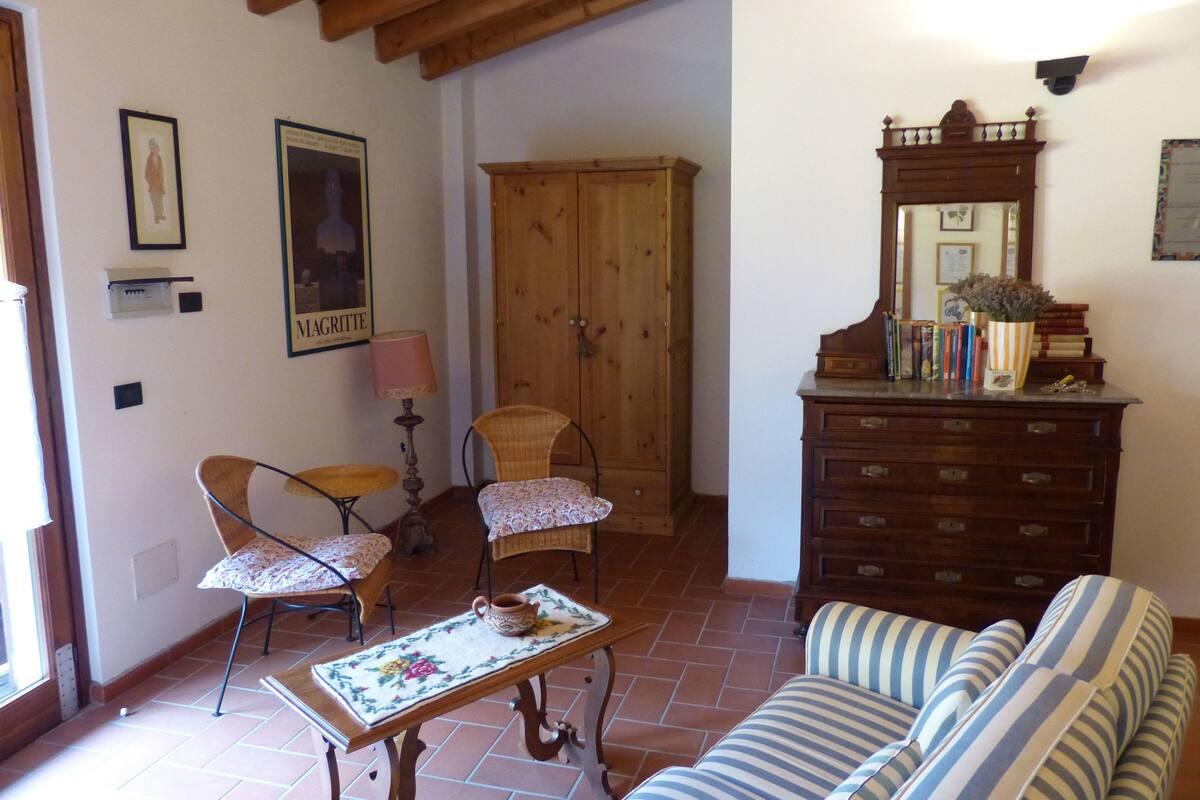A living room with a wooden cabinet, two wicker chairs, a striped sofa, and a tiled floor.