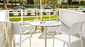 Un balcón con sillas y una mesa blancos, un vaso de agua y una cámara sobre la mesa.
