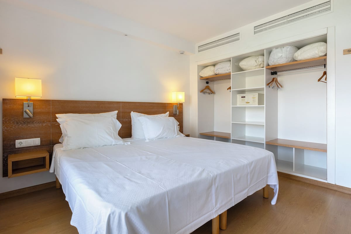 A hotel room with a large bed, bedside tables, a wardrobe with shelves, and a headboard.
