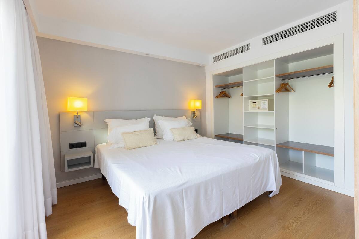 A hotel room with a large bed, bedside lamps, a wardrobe, and a small bedside table.