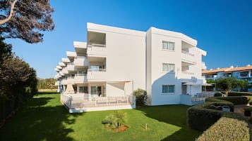 Un edificio moderno de varios pisos con balcones, un césped bien cuidado y un cielo azul despejado.