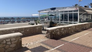 A beachfront restaurant with a clear view of the ocean, outdoor seating, and a stone wall. - The Beach House | Family Oasis (Fuengirola Al)