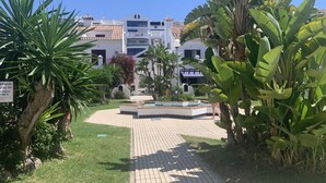 A courtyard with a pool, surrounded by palm trees and a building with a tiled roof. - The Beach House | Family Oasis (Fuengirola Al)