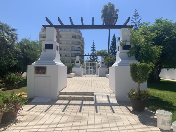 A gated entrance with a pergola, a paved pathway, and a building in the background.