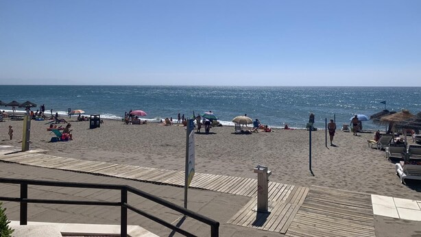 A beach with a wooden boardwalk leading to the water, umbrellas, and people relaxing. - The Beach House | Family Oasis (Fuengirola Al)