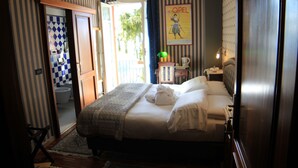 Habitació d'hotel amb llit, una taula de nit, una làmpada, una finestra amb cortines, una porta i vista a l'exterior.