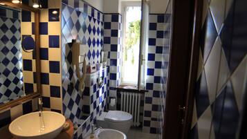 A bathroom with a checkered tile pattern, a sink, a toilet, and a window with a view of greenery outside.