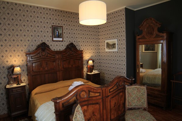 A traditional bedroom with a wooden bed, two bedside tables with lamps, a mirror, and patterned wallpaper.
