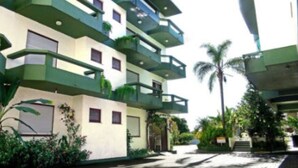 Un edificio de varios pisos con balcones, una palmera y una escalera que lleva a la entrada.