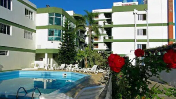 Un hotel con piscina, sillones de descanso y un jardín con flores rojas.