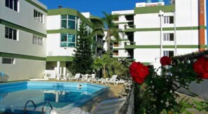 Un hotel con piscina, sillones de descanso y un jardín con flores rojas.