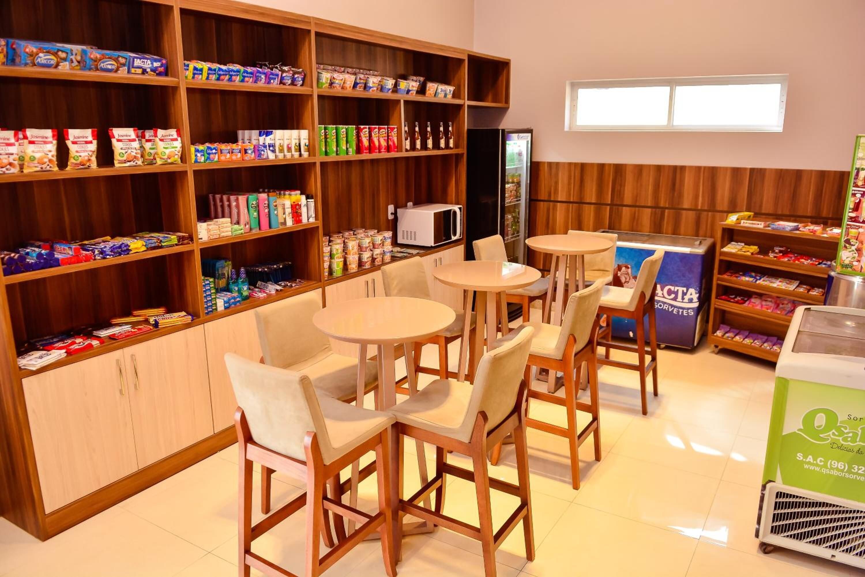 A snack bar with shelves stocked with various food items, a microwave, and seating area with chairs and tables.
