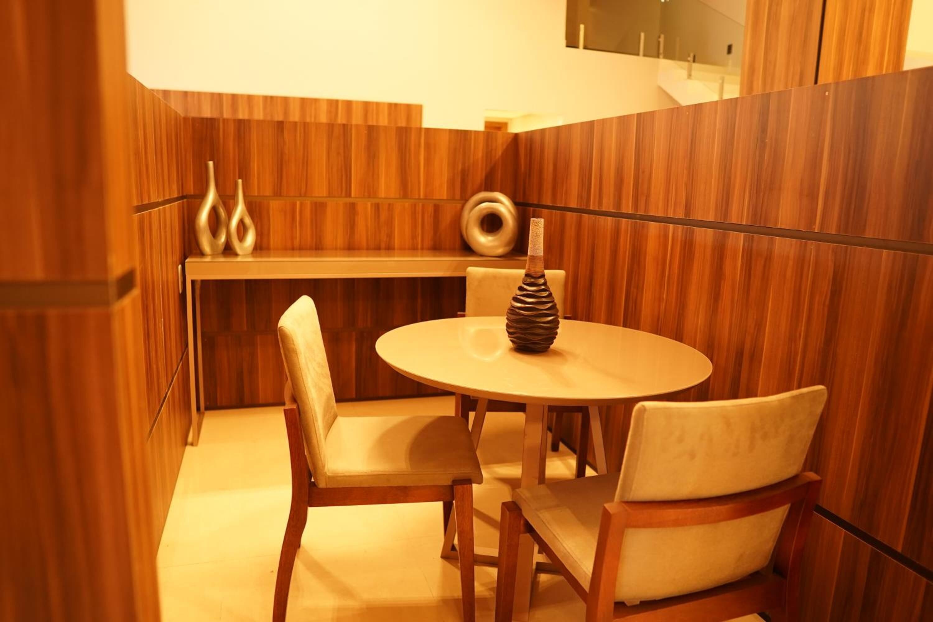 A small, cozy dining area with a round wooden table and two chairs, a decorative vase, and a wall-mounted shelf with vases.