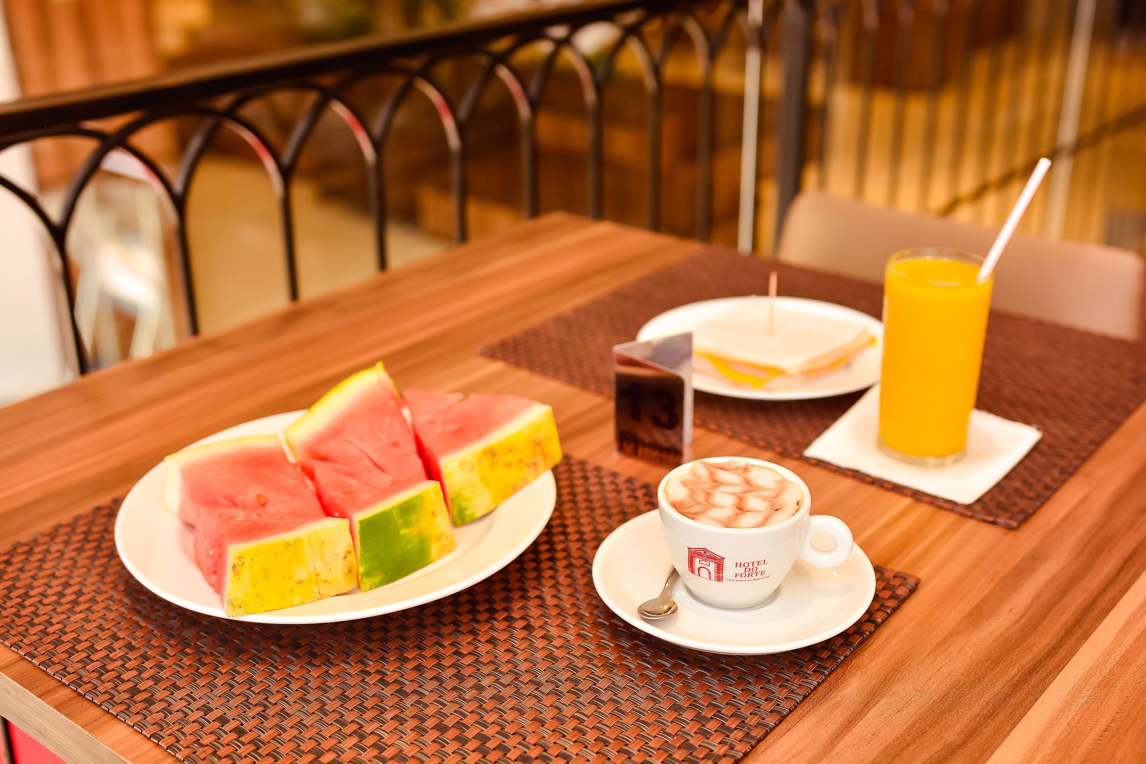 Mesa de madeira com fatias de melancia, uma xícara de café e um copo de suco de laranja.