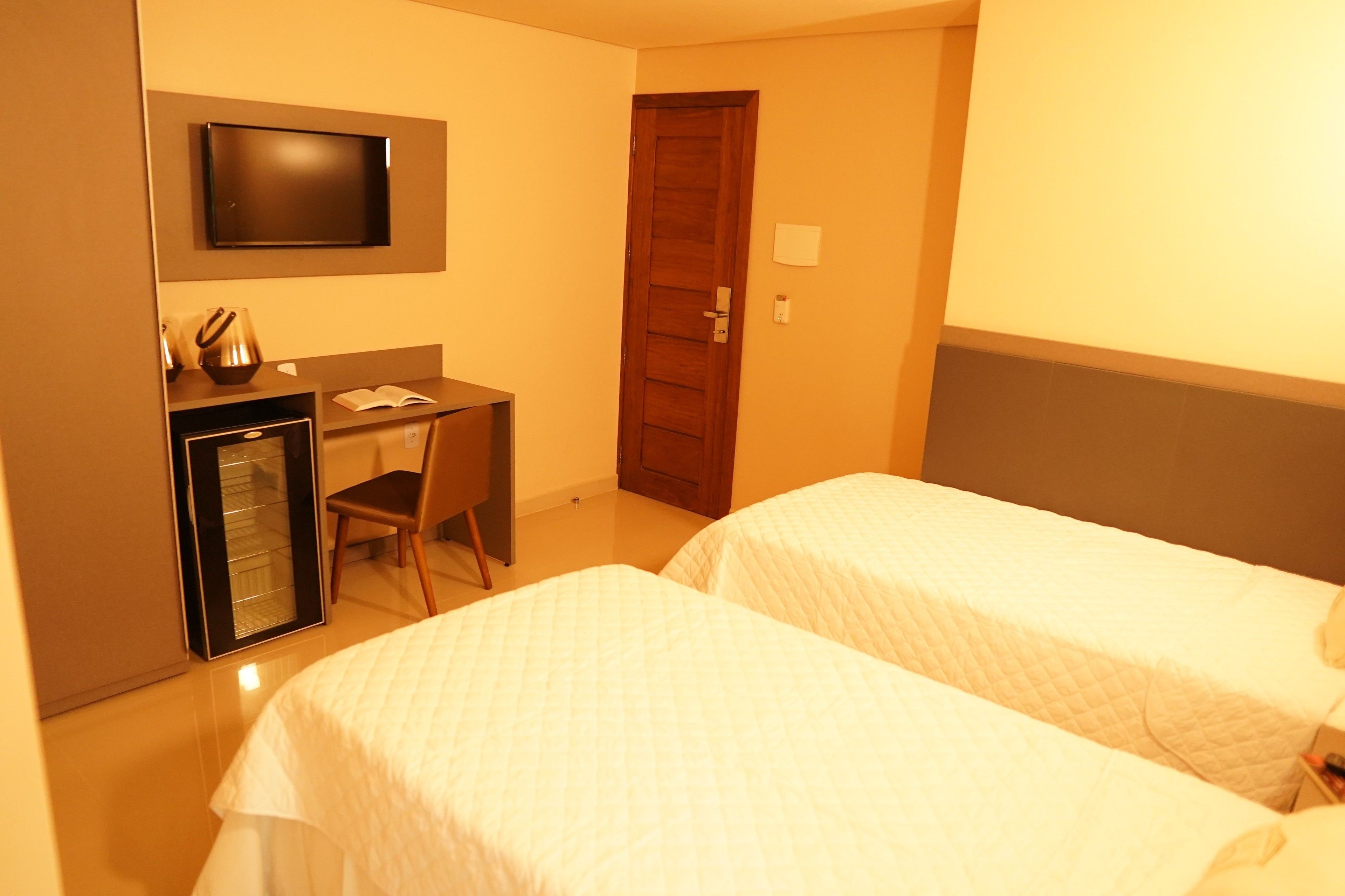 A hotel room with two beds, a desk, a chair, a television, and a door.