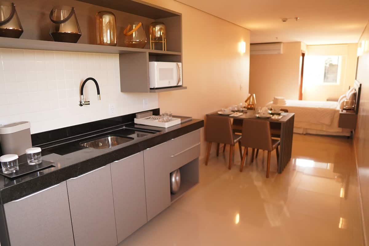 Una cocina moderna con encimera negra, pileta de acero inoxidable y muebles bajos blancos. Cuenta con un comedor con mesa y sillas.