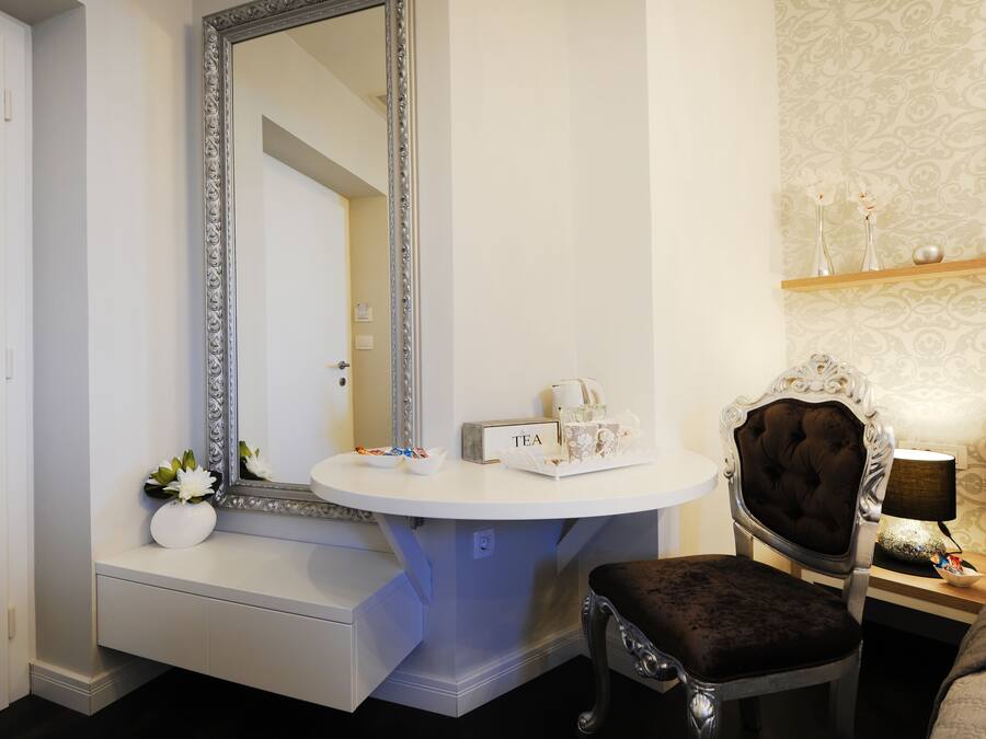A bathroom with a vanity, a mirror, a chair, and a shelf with toiletries.