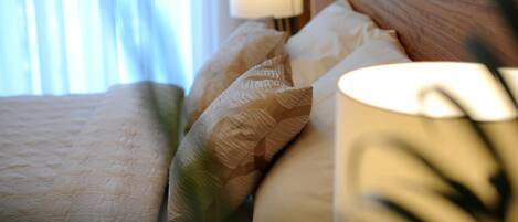 Una cama bien hecha con un edredón estampado y almohadas, una lámpara de noche y una ventana con cortinas.