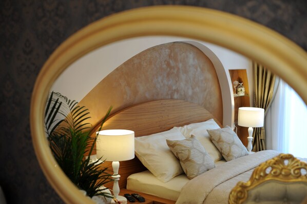 A bedroom with a large mirror reflecting the bed, bedside lamps, and a nightstand with a plant. - Silver & Gold Luxury Rooms (Zadar)