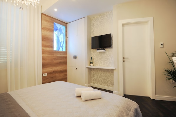 Une chambre d’hôtel avec un lit, un téléviseur fixé au mur, une porte en bois et une fenêtre avec des stores.