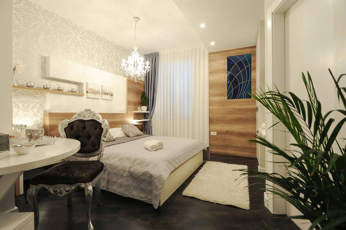 A modern bedroom with a bed, a vanity with a mirror, a chandelier, and a potted plant.