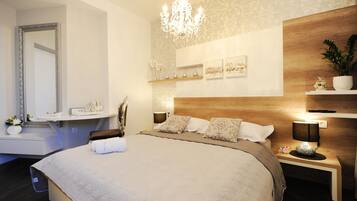 Un dormitorio moderno con una cama grande, un tocador con espejo, una araña y estantes de pared con objetos decorativos.