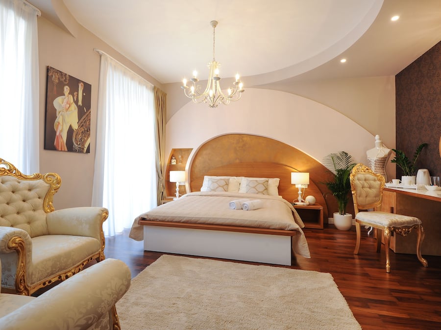 A luxurious bedroom with a large bed, ornate chairs, a desk, and a chandelier.