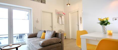 A modern living room with a grey sofa, yellow chairs, and a white dining table.