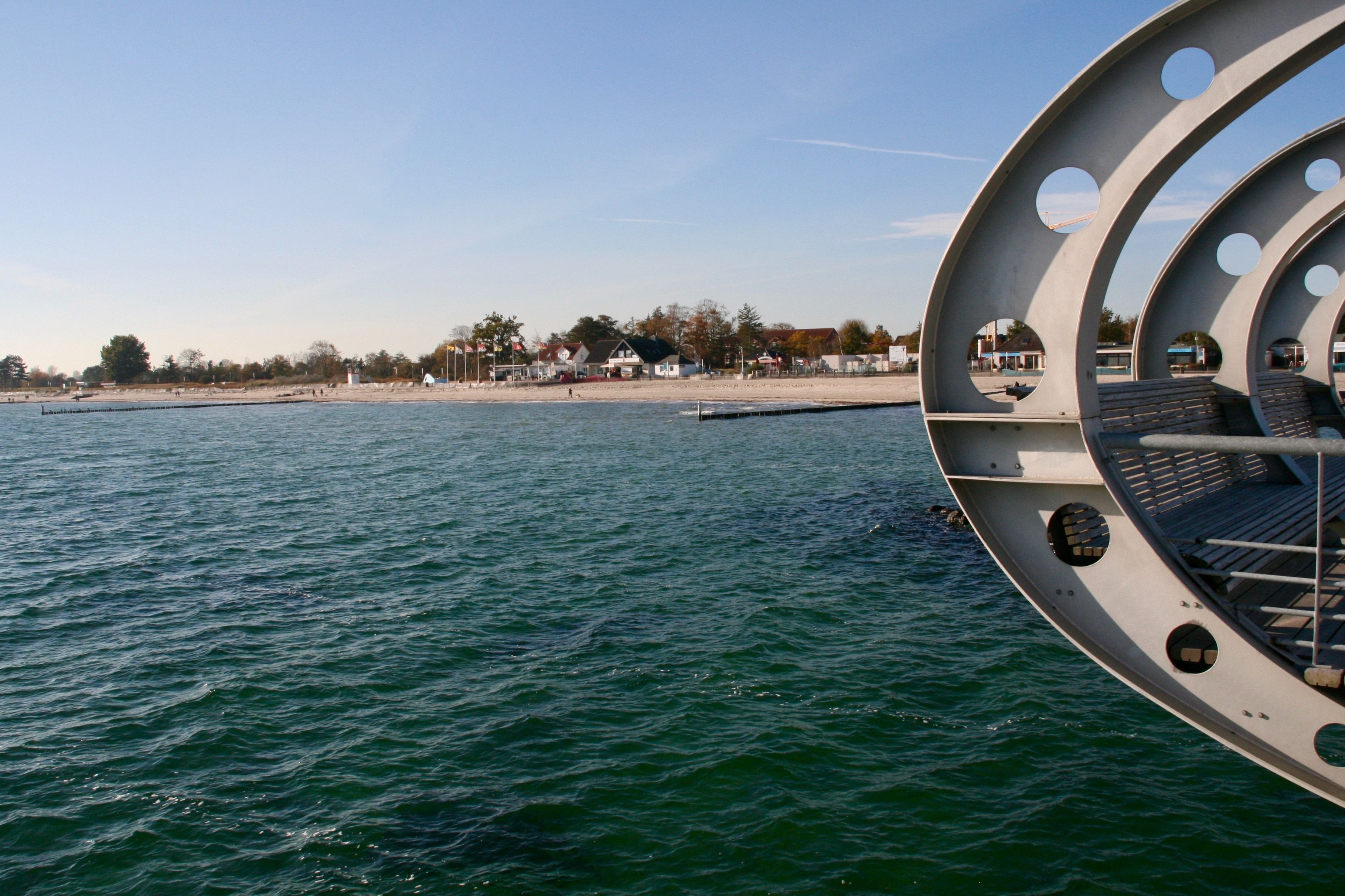 A boat with a circular deck and seating area, a sandy beach, and houses in the background.