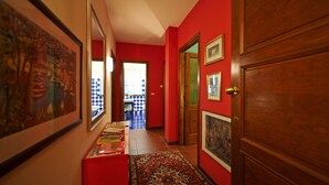 A hallway with red walls, wooden doors, and framed artwork. - Felicin - Dimora del Centro (Monforte d'Alba)