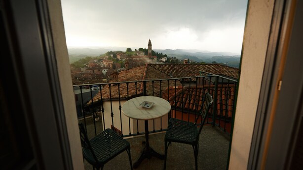 A balcony with a table and chairs, overlooking a town with a prominent tower. - Felicin - Dimora del Centro (Monforte d'Alba)
