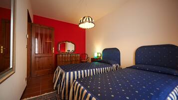 A bedroom with two beds, a wooden wardrobe, a mirror, and a hanging light fixture.