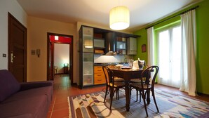 A dining area with a table and chairs, a hanging light fixture, and a view of a green wall and window with curtains. - Felicin - Dimora del Centro (Monforte d'Alba)