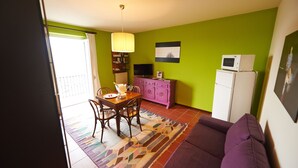 A compact living space with a dining area, a purple sofa, a kitchen with a microwave, and a TV. - Felicin - Dimora del Centro (Monforte d'Alba)