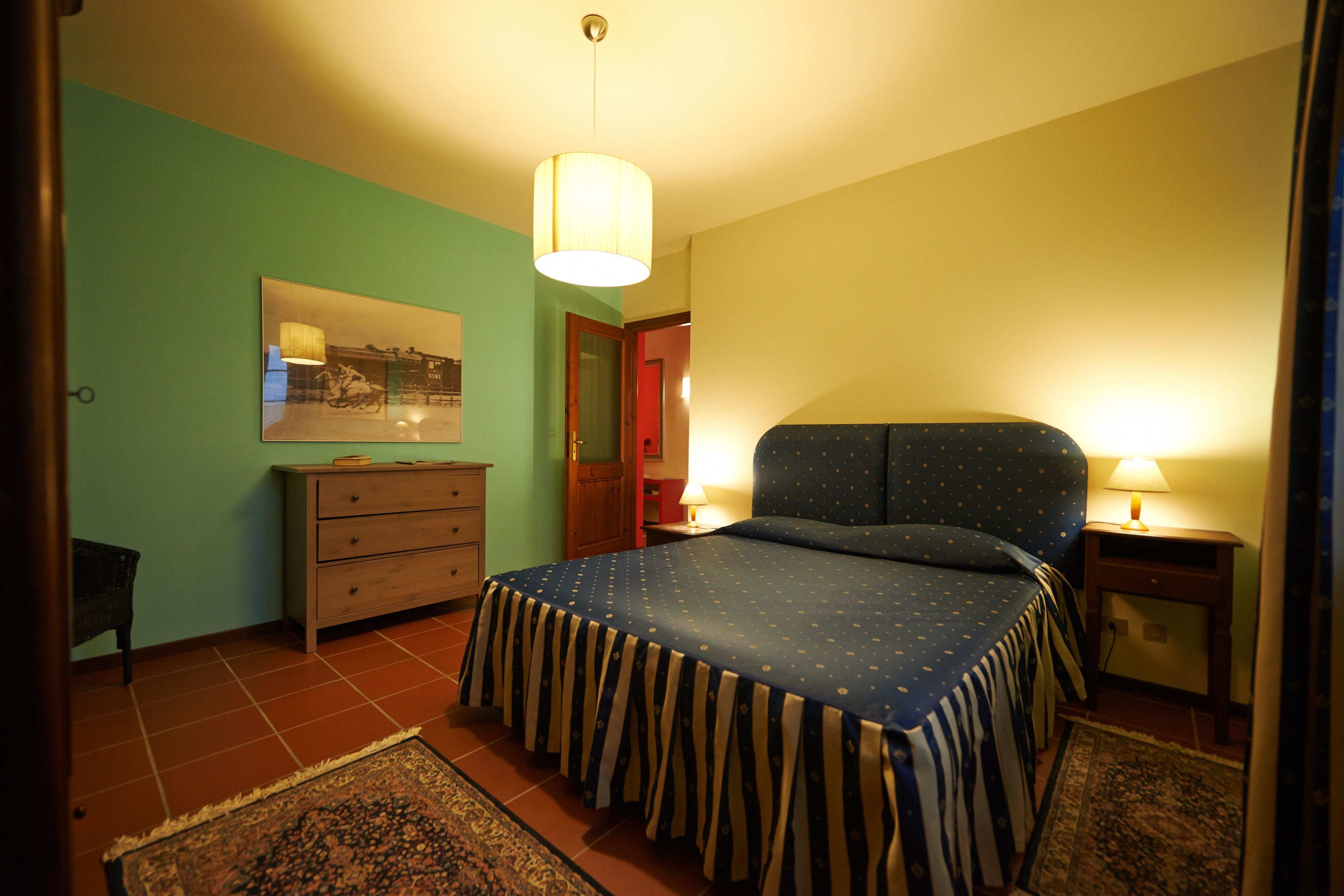 Une chambre à coucher avec un lit, une commode, une chaise, un tapis et un tableau accroché au mur.