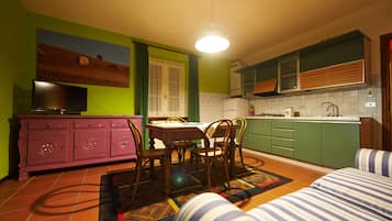 A compact kitchen with a dining area, green walls, and a television on a cabinet.