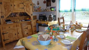 A dining area with a table set for breakfast, a wooden cabinet with decorative items, and a view through the window. - B&B Les Acacias (Bagnes)