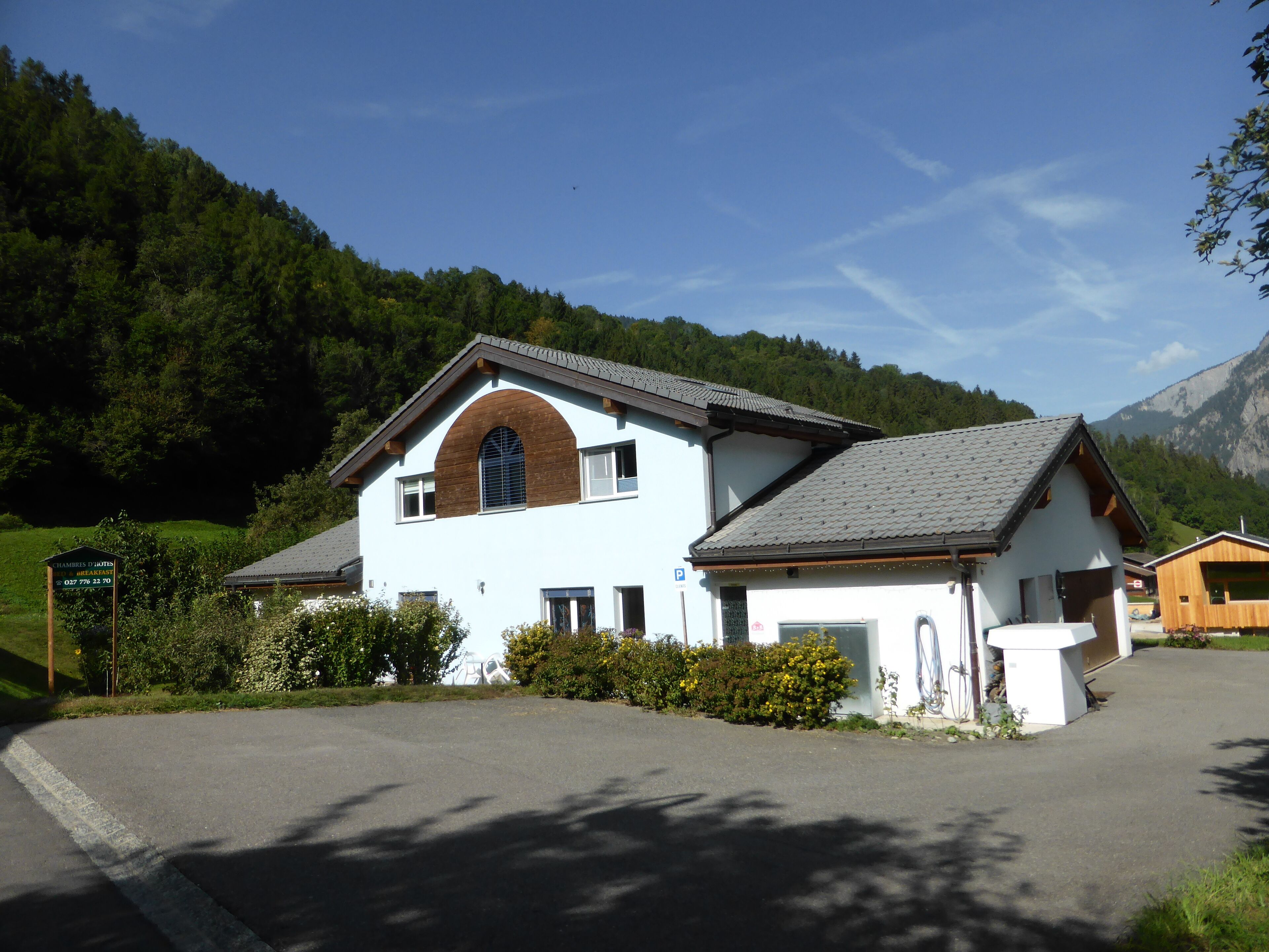 A two-story building with a sloped roof, a central arched window, and a small attached structure with a wooden facade.