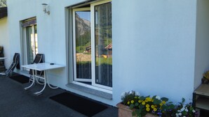 A white building with a large sliding glass door, a small window, and a white table with chairs outside. - B&B Les Acacias (Bagnes)