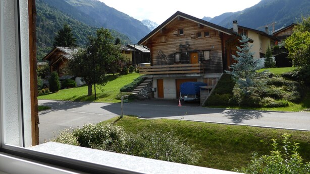 A wooden chalet with a balcony, surrounded by lush greenery and mountains. - B&B Les Acacias (Bagnes)