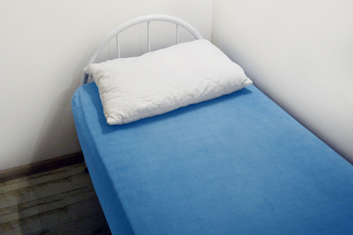 A small, single-bed room with a blue mattress and a white pillow.