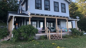 A two-story house with a covered porch, a satellite dish, and a wooden deck. - Ocean-Beach Front Cottage on Blue Hill Bay w/ Mt Desert Island on the Horizon... (Surry)