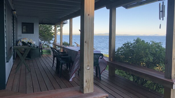A wooden deck with outdoor seating, a table, and a view of a lake. - Ocean-Beach Front Cottage on Blue Hill Bay w/ Mt Desert Island on the Horizon... (Surry)